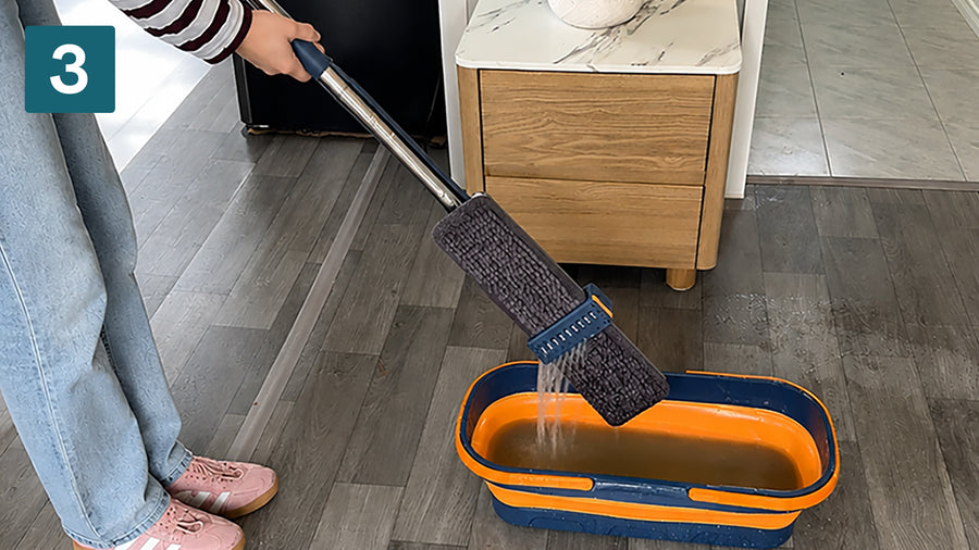 Wringing the microfibre mop pad dry over the bucket scrapers without touching the water